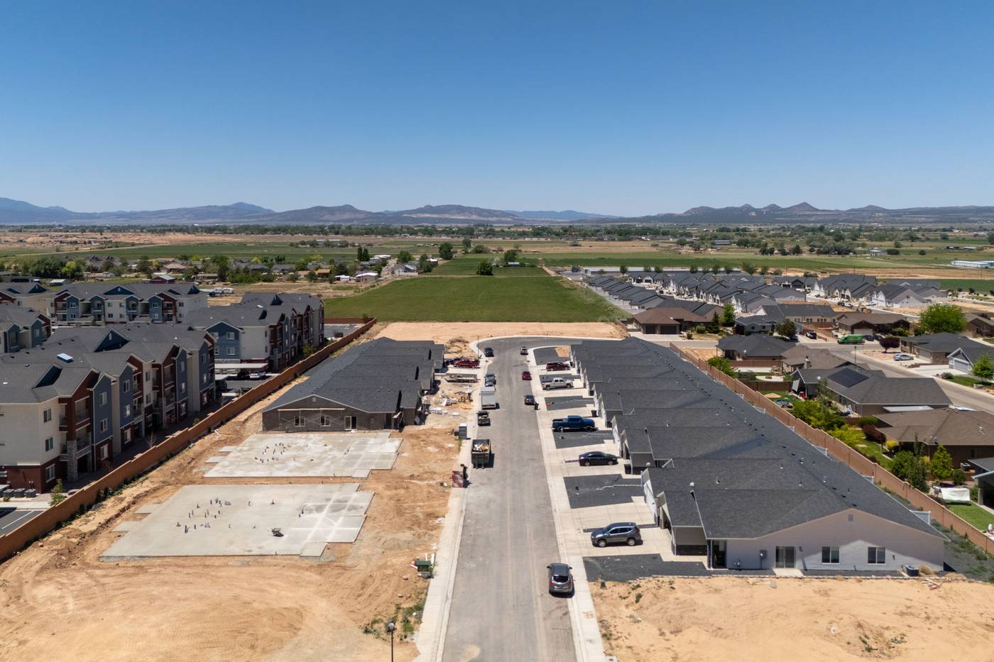 Aerial view along the Old Farms street showing finished single-level homes on one side and poured foundations on the other.