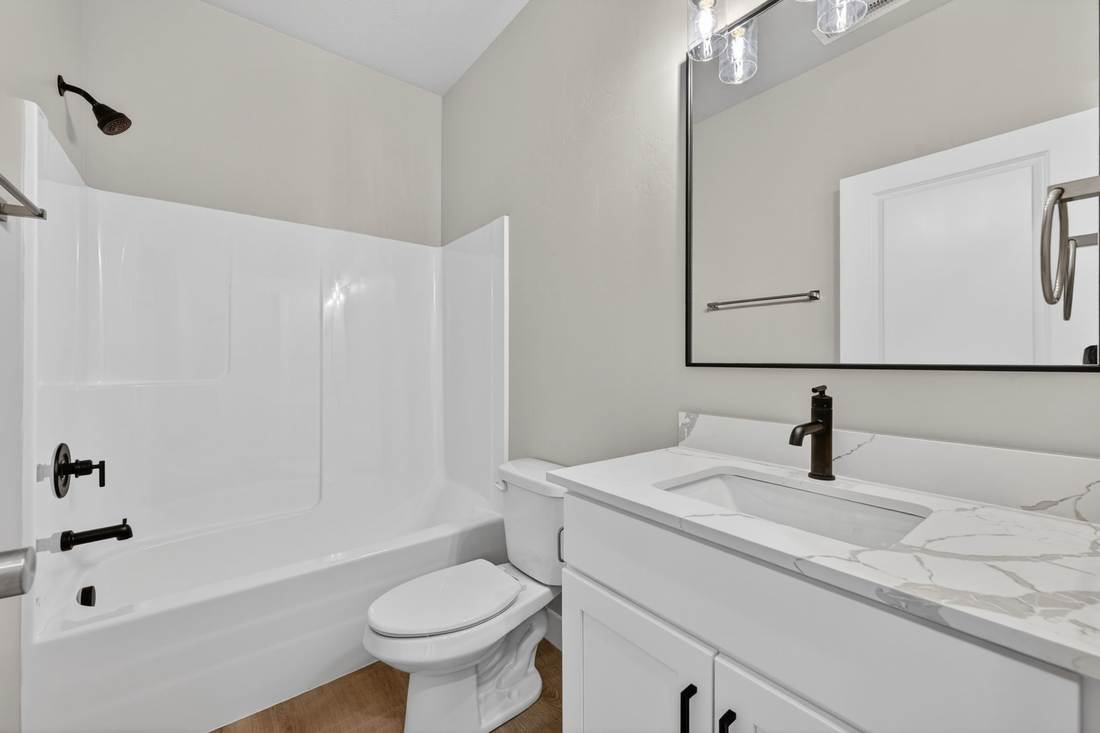 Full bathroom with tub and shower surround, quartz-topped vanity, black fixtures and a framed mirror.