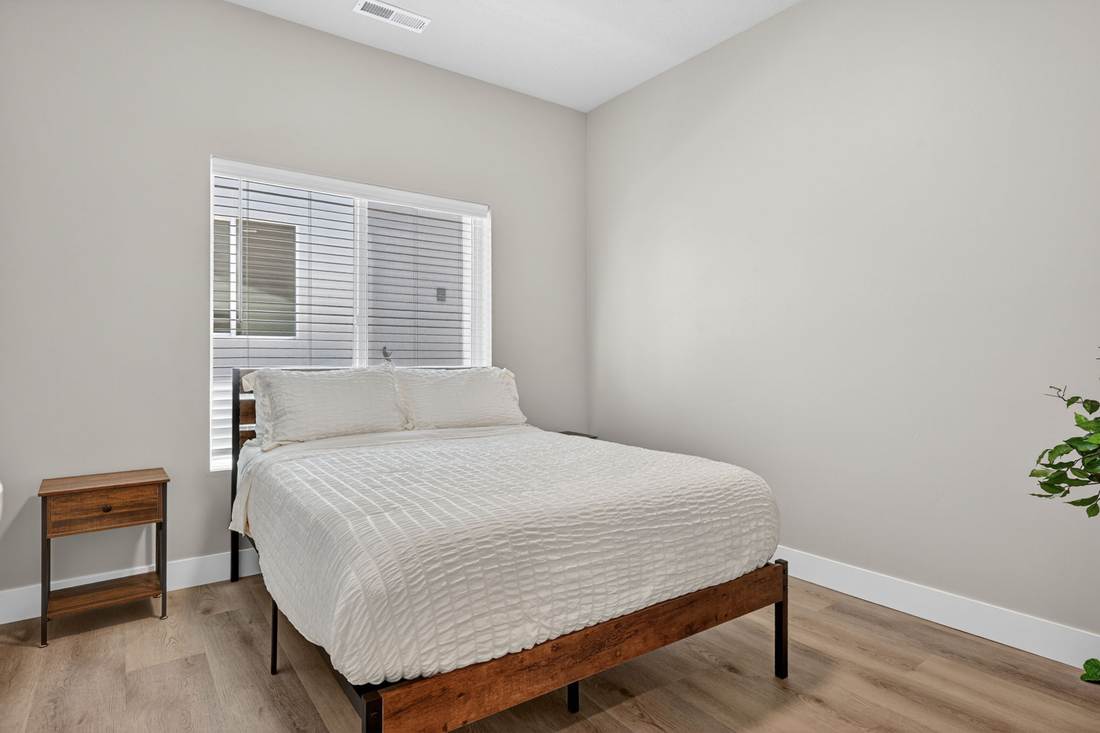 Second bedroom with queen bed beneath a wide window, nightstand and plant.