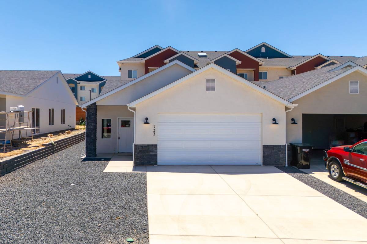 Front of the home with white garage door, stone wainscot, gooseneck lights and the house number 133.