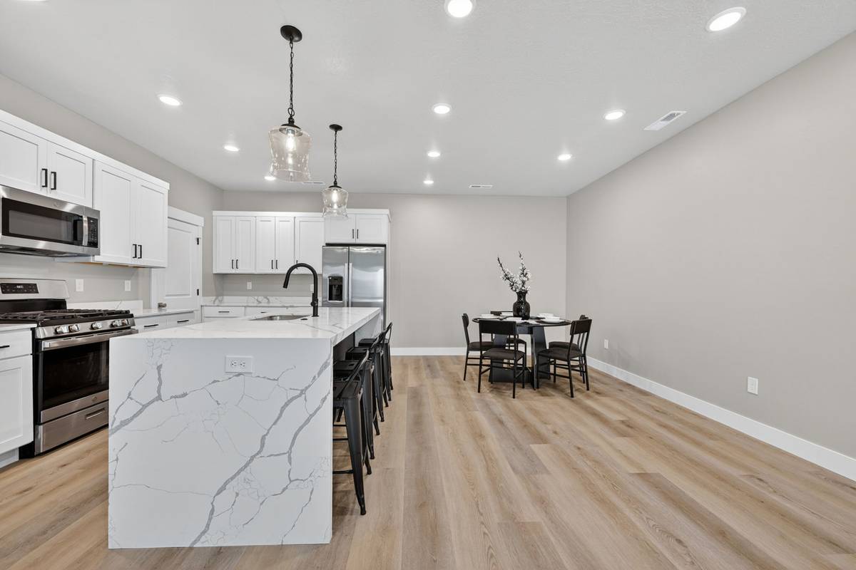 Kitchen with white cabinetry, quartz island with pendant lighting, and a round dining table beyond.