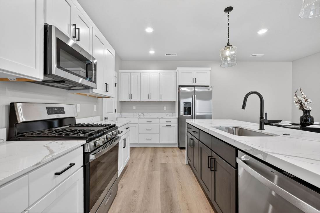 Stainless gas range and over-range microwave against quartz counters, with the island sink and dishwasher opposite.