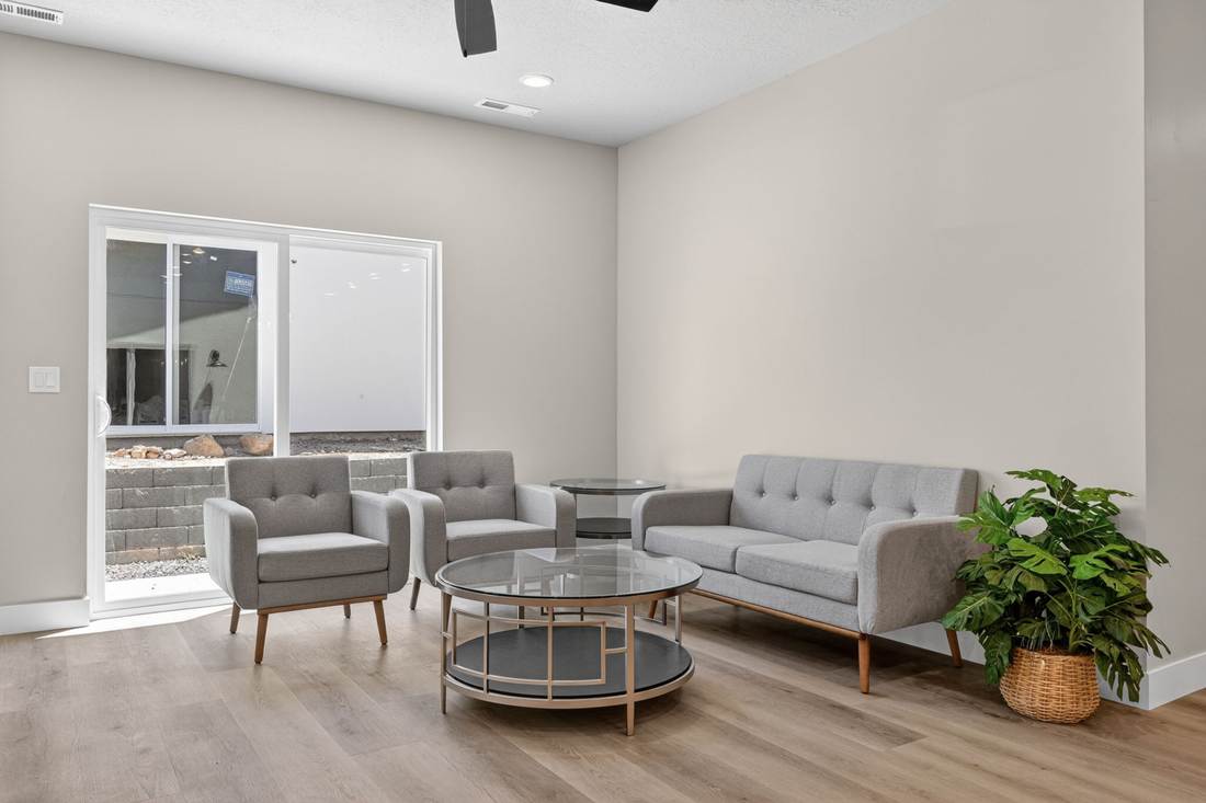 Living area with two armchairs, a sofa, potted plant, and a sliding glass door to the rear yard.