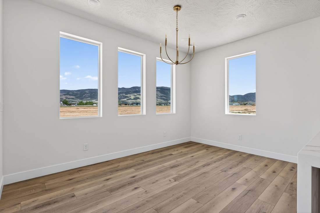 Dining room with a brass chandelier and four tall windows looking out to farmland and mountains.
