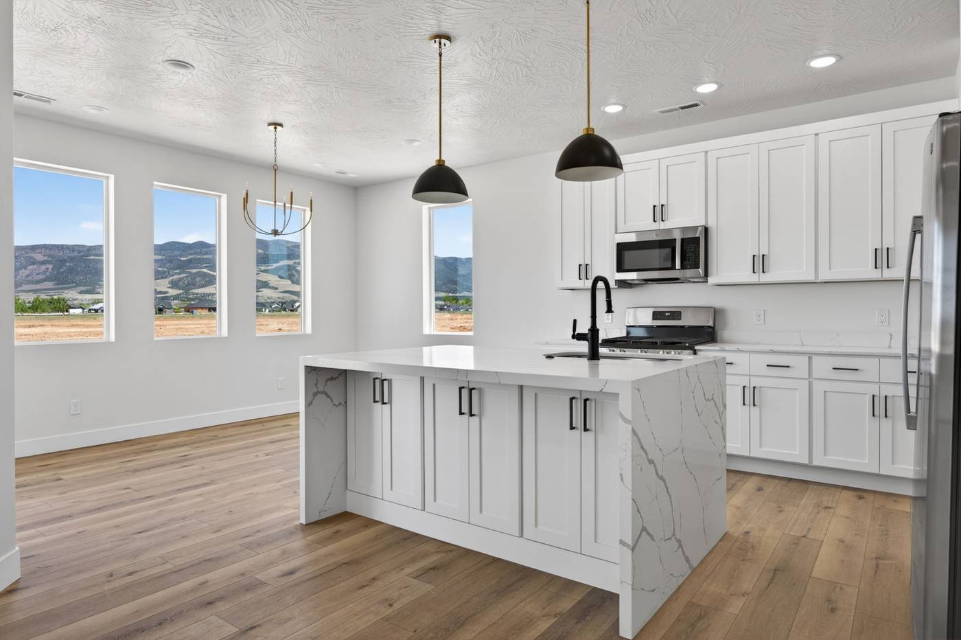 Kitchen with waterfall quartz island and black pendants, opening to a dining area with four windows framing the mountains.